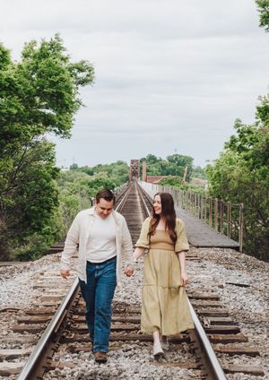 Romantic couple photoshoot on rustic railroad tracks surrounded by greenery.