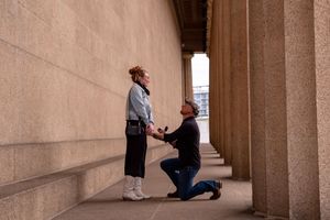 Proposal moment captured in stone colonnade with dramatic natural lighting.