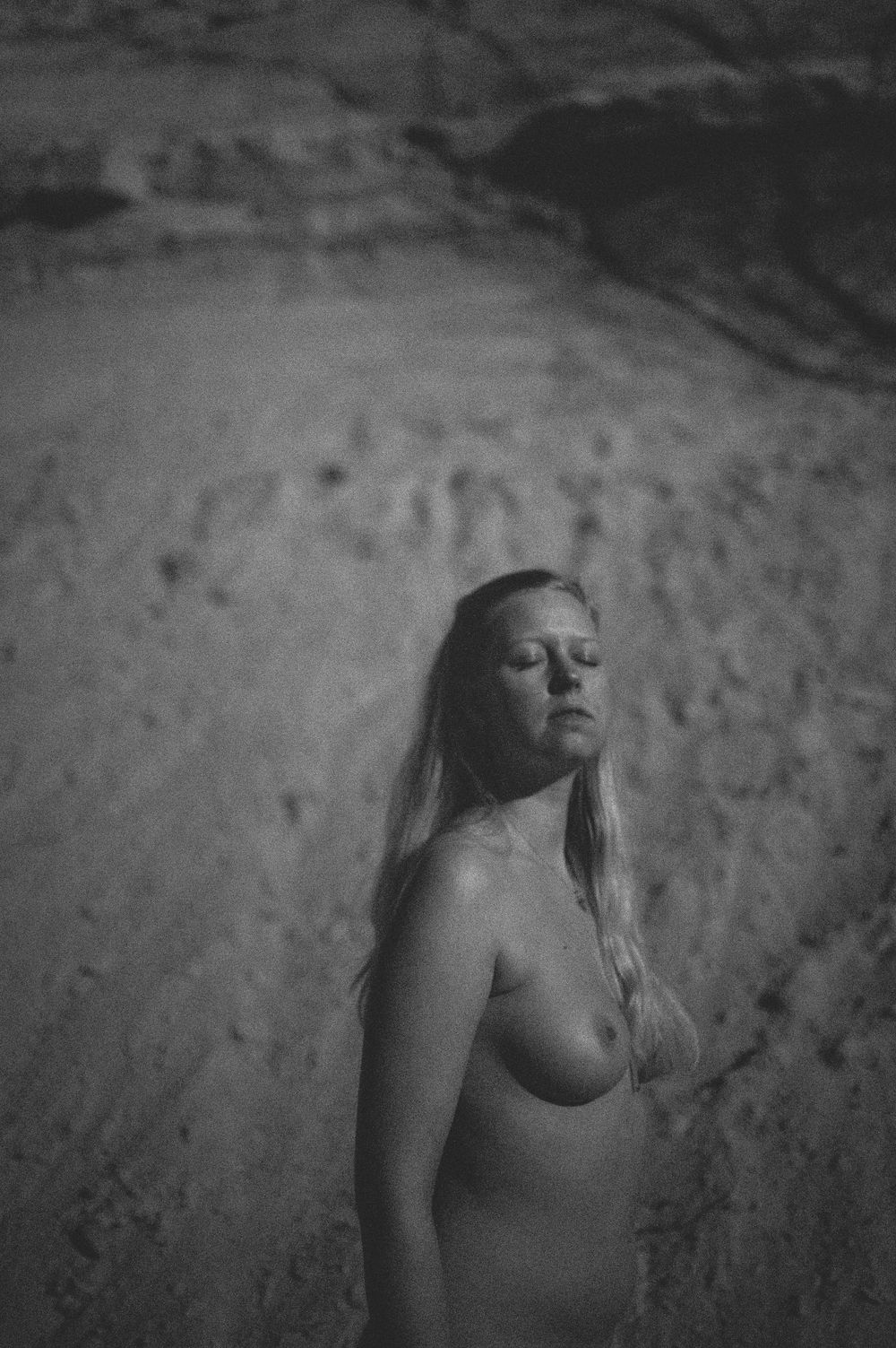 Artistic black and white photograph of a bare figure against a textured stone or rock wall background.
