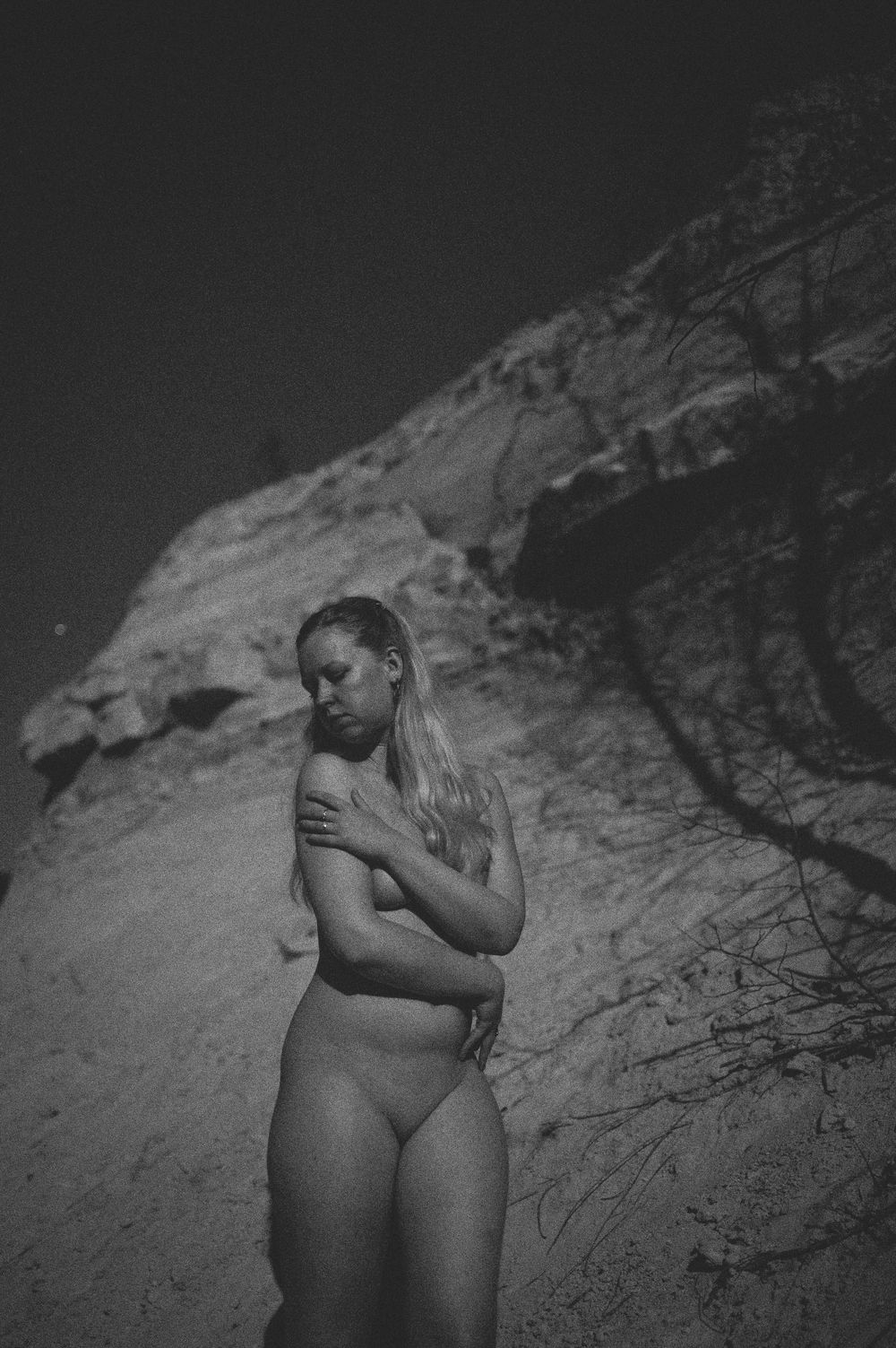 Artistic black and white portrait of a figure against textured rock formations in nature.