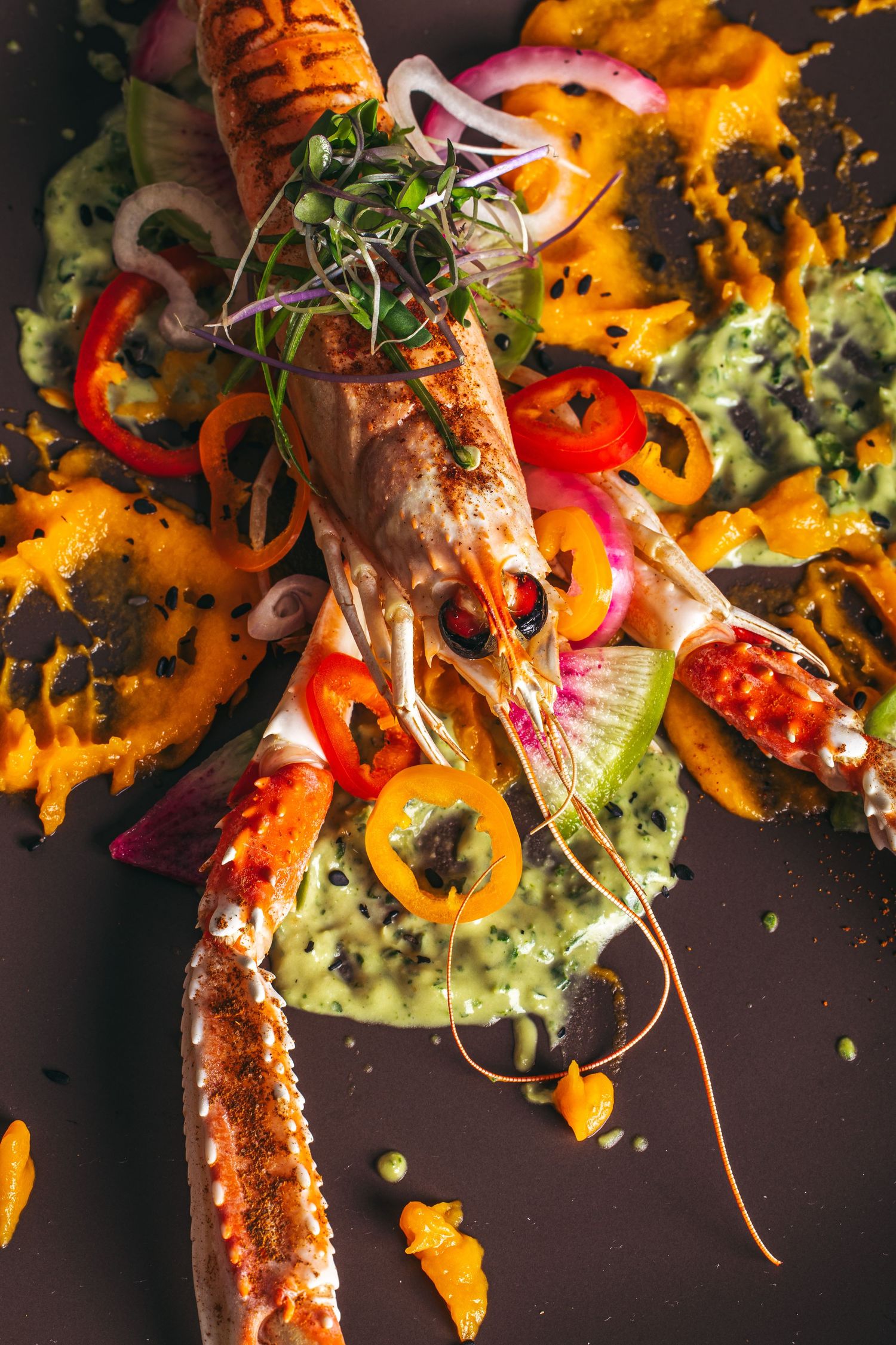Colorful plate of grilled meat with vibrant bell peppers, microgreens and orange sauce artfully presented.