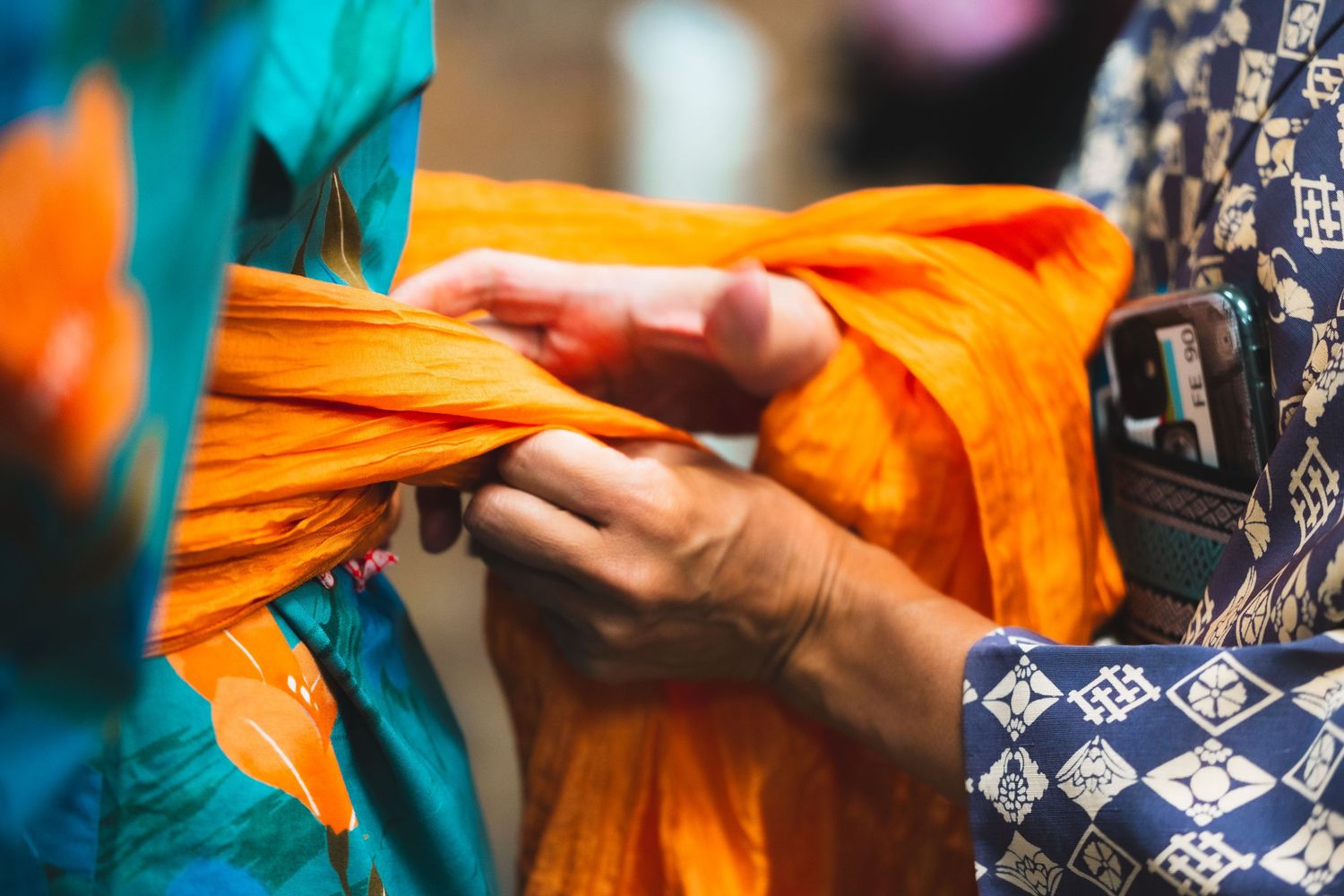 Hands folding orange fabric with blue geometric patterns.