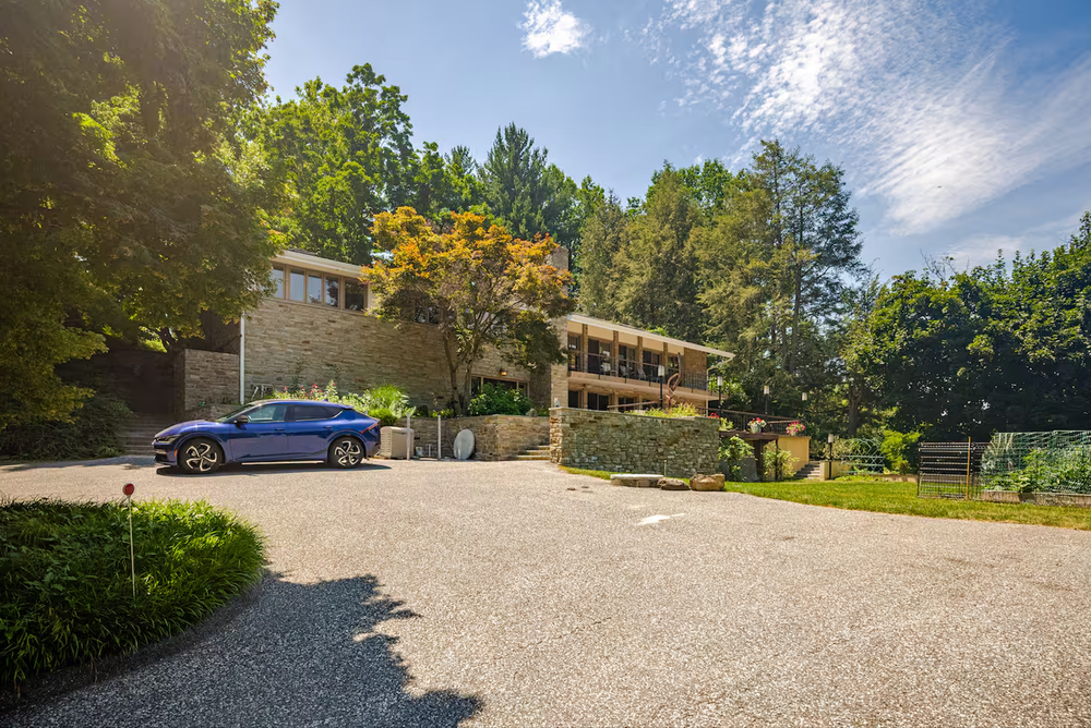 Luxury estate exterior in Baltimore County featuring manicured gardens and Tesla in driveway.