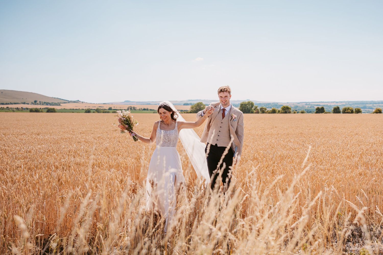 A couple walks together through a golden wheat field on a sunny summer day.