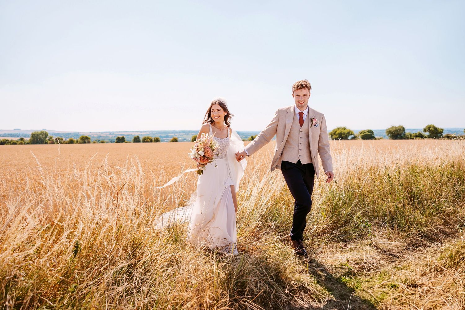 A couple walks hand in hand through a golden wheat field at sunset creating a romantic silhouette.