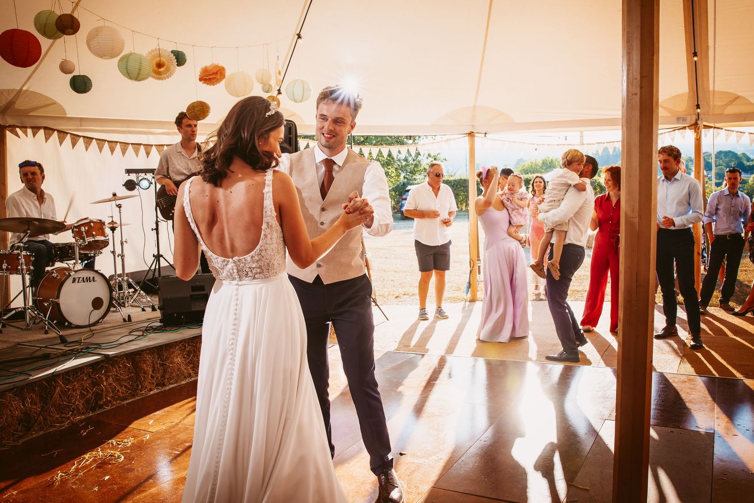 Wedding guests dance and celebrate under paper lanterns and string lights at an indoor reception venue.