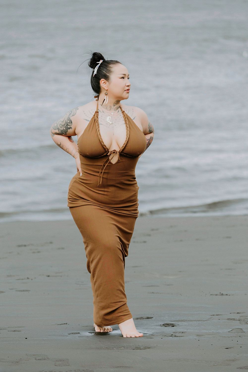 Woman in brown dress poses confidently on misty beach.