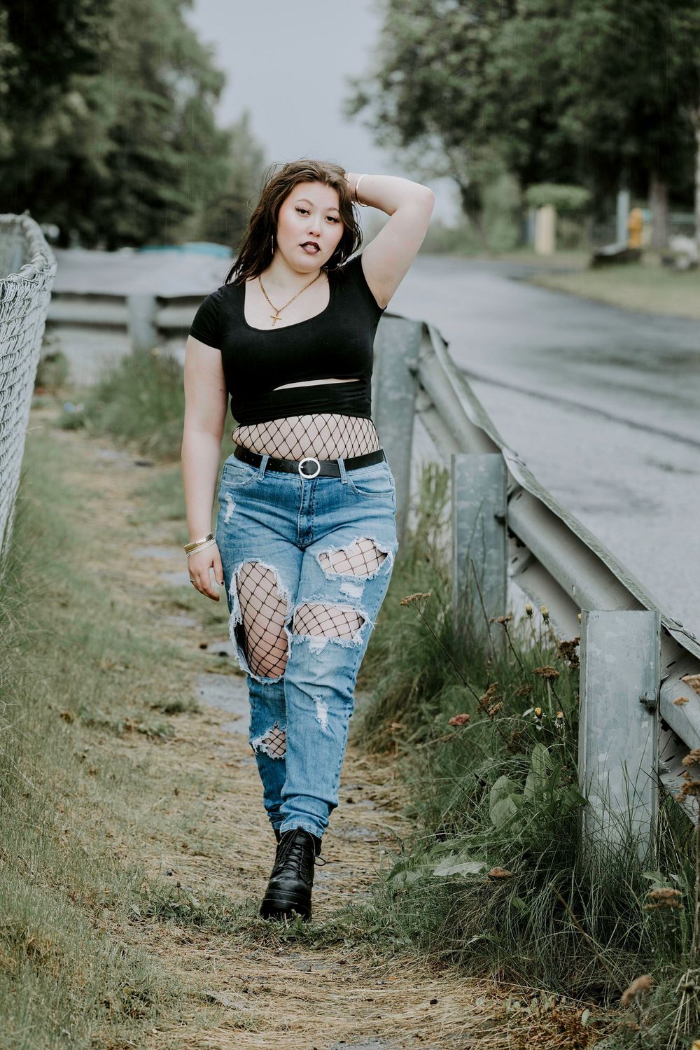 Alternative style fashion photo on rural path with black crop top, distressed jeans with fishnet and combat boots.