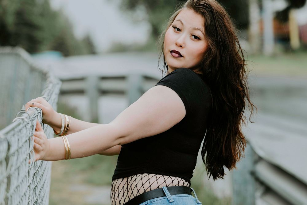 Person in fishnet stockings and black dress leaning against white fence in outdoor setting at sunset.