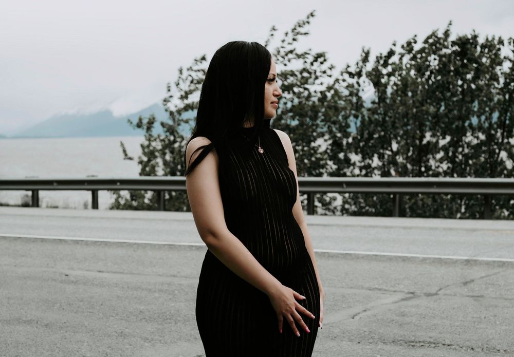 Silhouette of a person in black dress standing near a railing with mountains in the background.