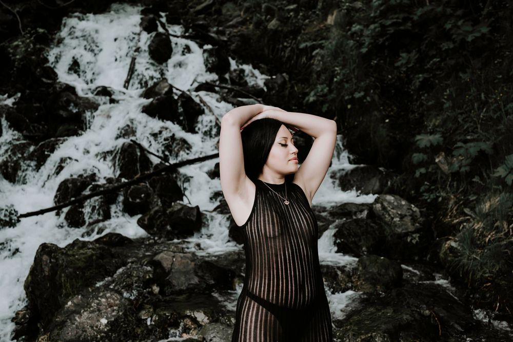 Dramatic pose against waterfall wearing black sheer outfit.