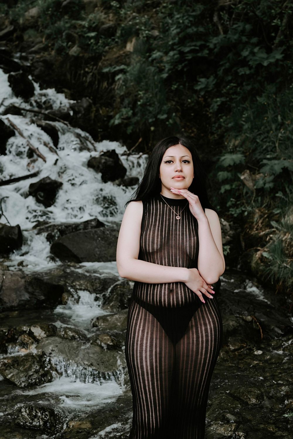 Artistic portrait by waterfall wearing sheer black dress.