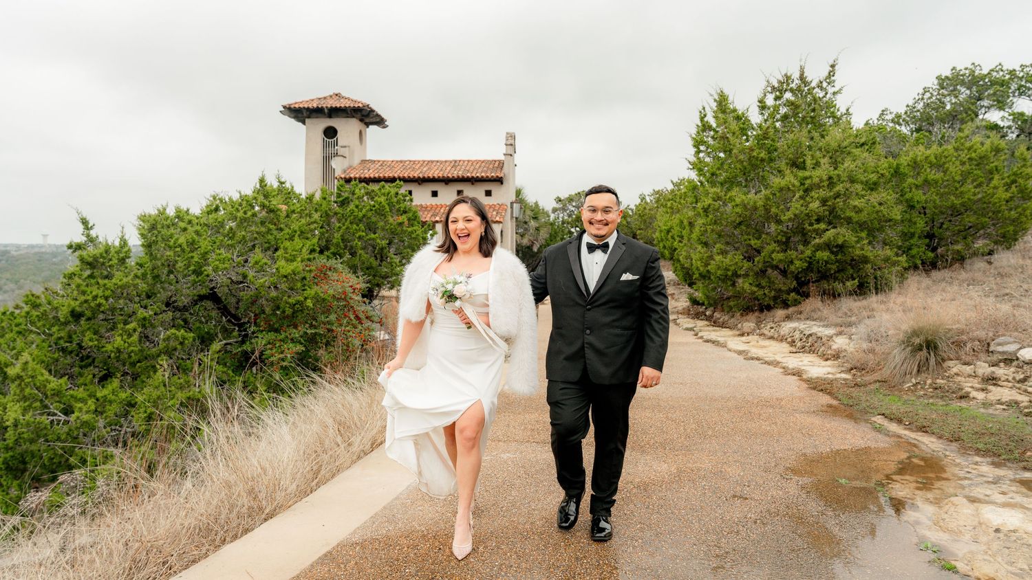 Newly wedded couple smiling in Austin wedding venue surrounded by green brush and beige rocks.