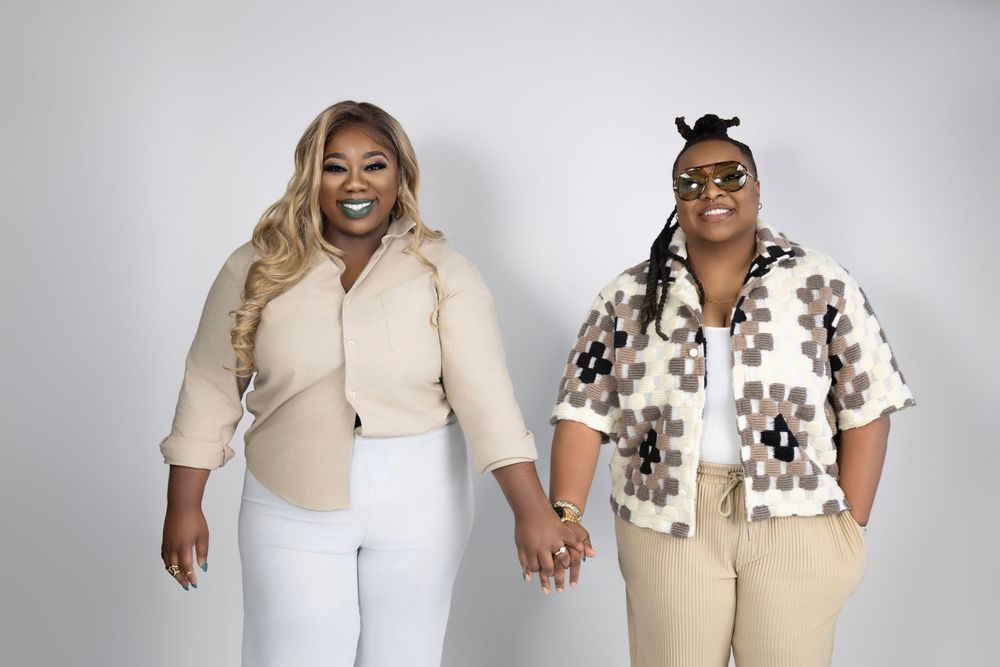 Two people pose in matching cream colored outfits and black and white patterned shirts, showing off their coordinated style.