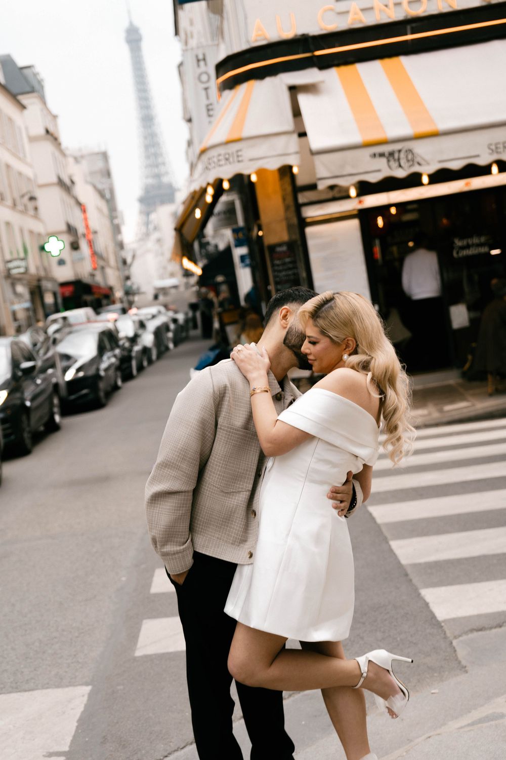 Romantic couple embracing on a Paris street with the Eiffel Tower visible in the background.