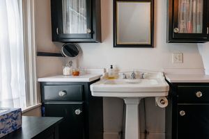 Modern bathroom interior with black cabinets, white pedestal sink, and natural light streaming through window.