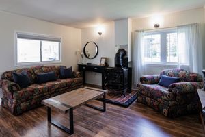 A bright living room features floral print sofas, hardwood floors, and a wooden coffee table near large windows.