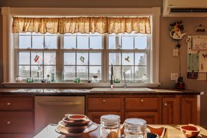 Sunlit kitchen window with brown cabinets and decorative valance showcasing distant mountain views.