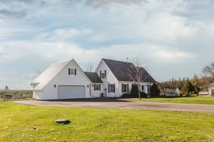 A scenic panoramic view of white residential houses with garages nestled alongside a green grassy field on a cloudy day.