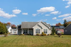 Single-story beige ranch home with gray roof, arched windows, and lush green lawn under a bright blue sky.