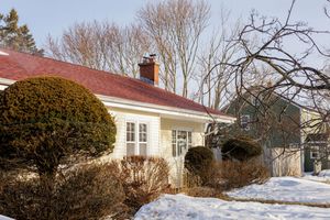 White ranch-style house with red roof and trimmed shrubs in winter snow landscape.
