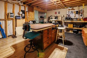 A well-organized woodworking workshop with a large workbench, tools, and exposed wooden beams on the ceiling.
