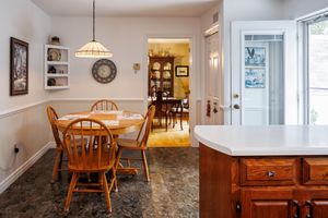 Light-filled dining room with wooden chairs, circular table and marble kitchen island connected to adjacent rooms.