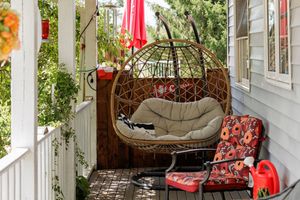 Cozy hanging egg chair with cushions on a white porch features floral patterned pillows and red accents.