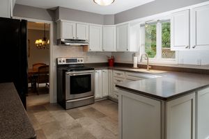 White kitchen cabinets with stainless steel appliances and dark countertops show a modern renovation in progress.