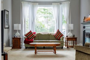 Bright living room with bay window, green sofa, red striped pillows, matching side tables and sheer white curtains.