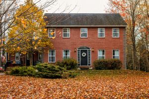 Red Colonial house with fall foliage and scattered orange leaves across the yard.