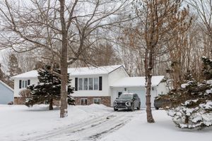 Snow covered split-level home with white exterior and silver SUV parked in driveway during winter season.