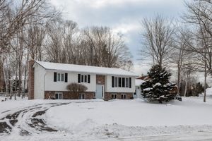 White split-level ranch house with black shutters on a snowy winter day surrounded by bare trees and evergreens.