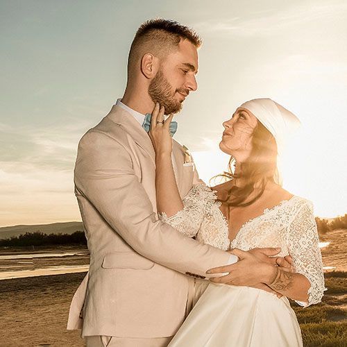 Romantic couple embraces on a sunlit beach at golden hour, showcasing tender moments in their formal attire.