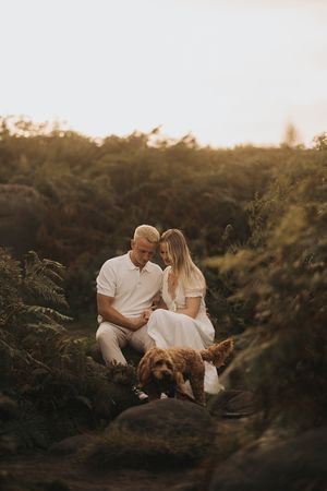 A romantic sunset moment between a couple and their dog sitting among ferns and foliage in warm golden light. By Lincolnshire photographers.