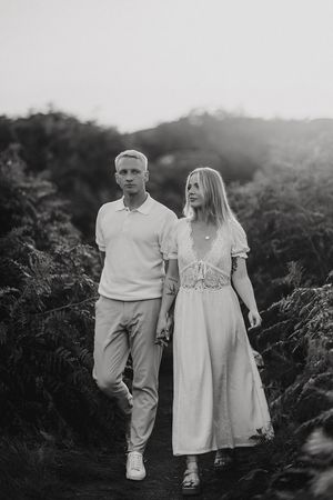 Black and white photo of a couple walking together on a nature path surrounded by ferns at twilight. Captured by Lincolnshire photographers.
