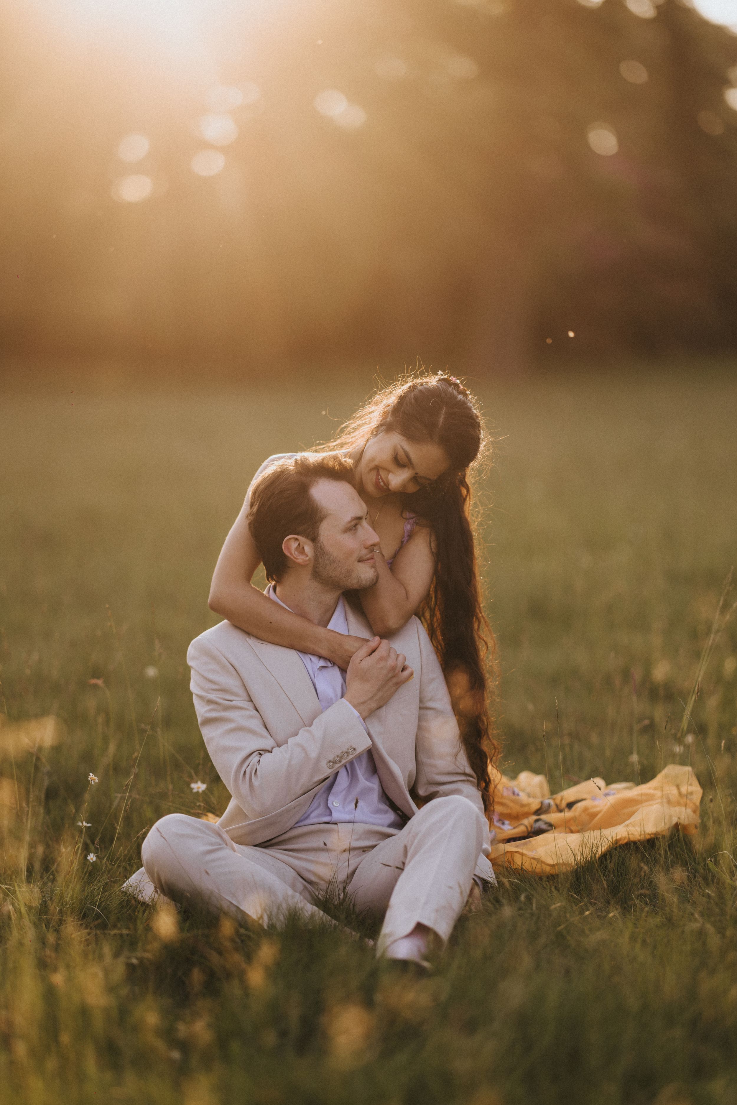 A romantic couple lies together in a sunlit meadow during golden hour. Image captured by Lincolnshire photographers.