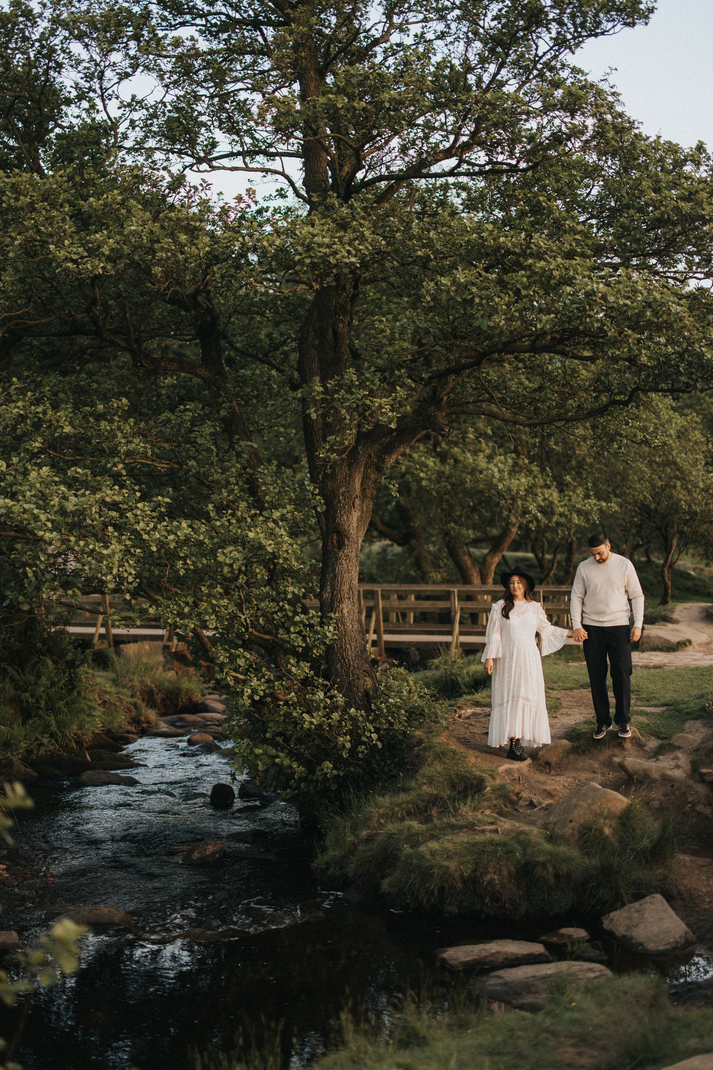 Couple walks along a scenic wooded stream with rocks and trees in a romantic natural setting. Captured by Lincolnshire photographers.