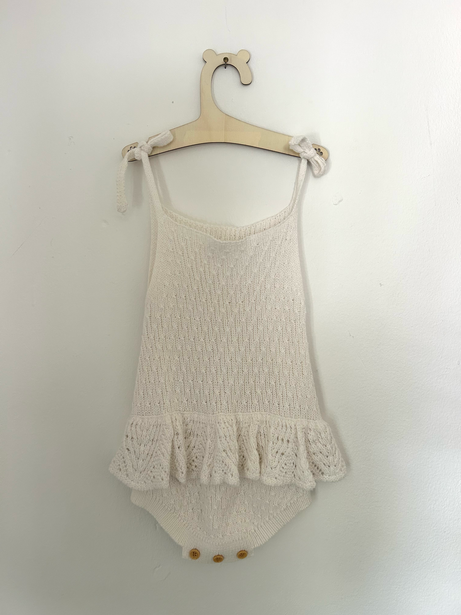 White baby romper with delicate pink embroidered floral design and ruffle details on straps.