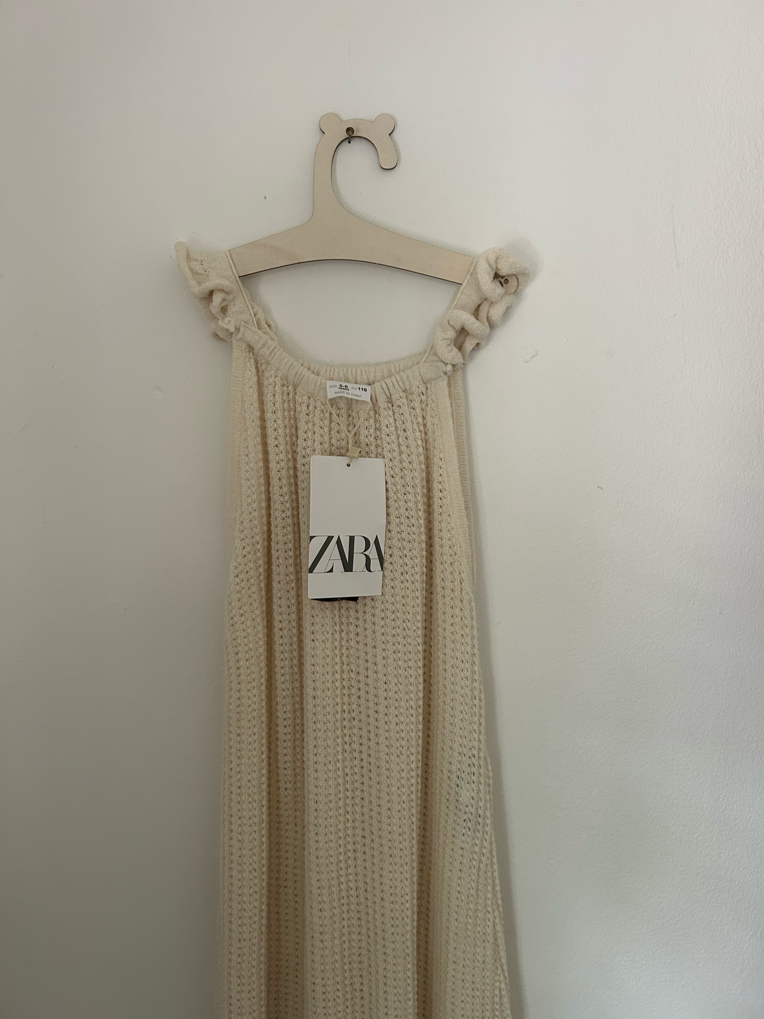 White knit baby romper with 'ONE' text and small bow detail in pink embroidery against hanging clothing background.
