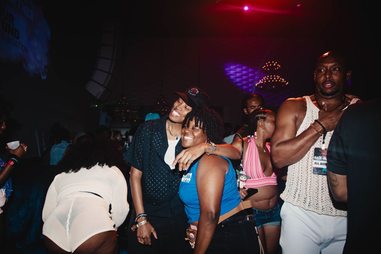 People dancing and enjoying themselves at a dark nightclub with colorful lights in the background.