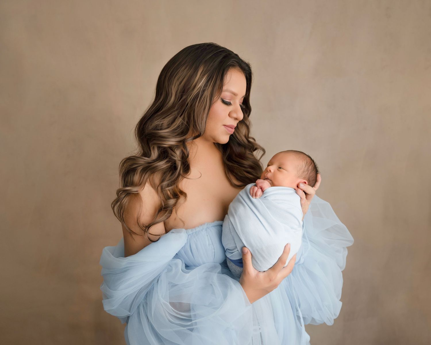 Mother and newborn baby portrait in matching powder blue outfits against neutral background.
