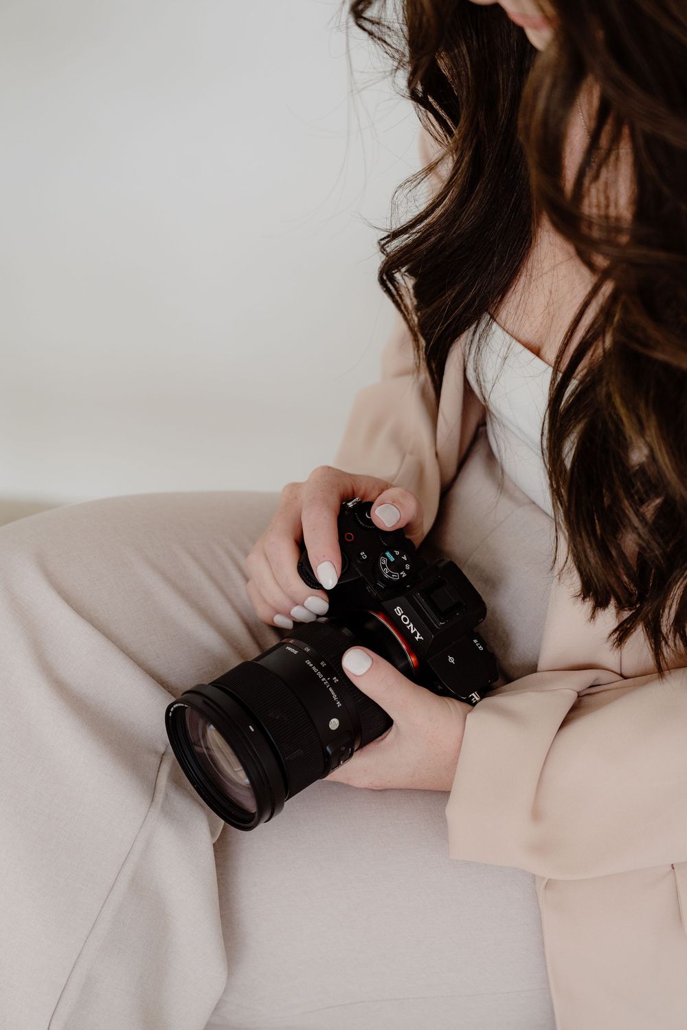Close up of hands holding professional camera while wearing neutral toned clothing.