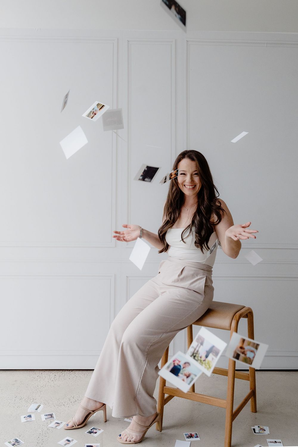 Woman in neutral outfit tossing polaroid photos in white studio setting.