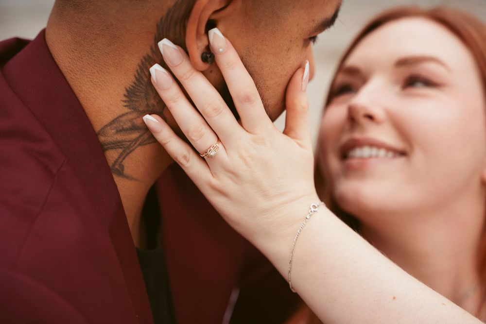 Woman showing her engagement ring while embracing her partner in a burgundy shirt during a romantic moment.