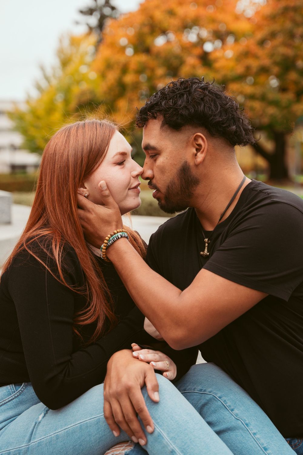Romantic couple in casual wear sharing an intimate moment against autumn foliage background.