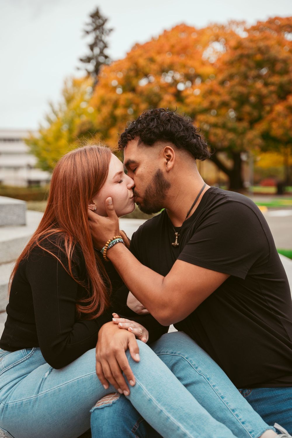 Romantic couple sharing an intimate kiss on steps surrounded by autumn foliage.