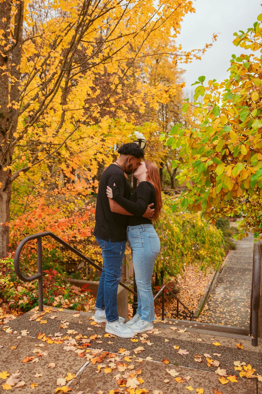 A couple shares an intimate moment on stone steps surrounded by vibrant autumn foliage.