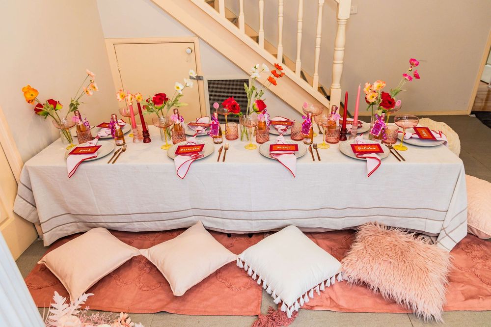A long elegant dining table set with pink cushions, white decor, floral arrangements, and tableware.