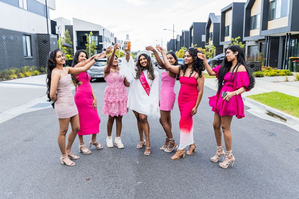 A group of bridesmaids in bright pink dresses walking together on a residential street for wedding photos.
